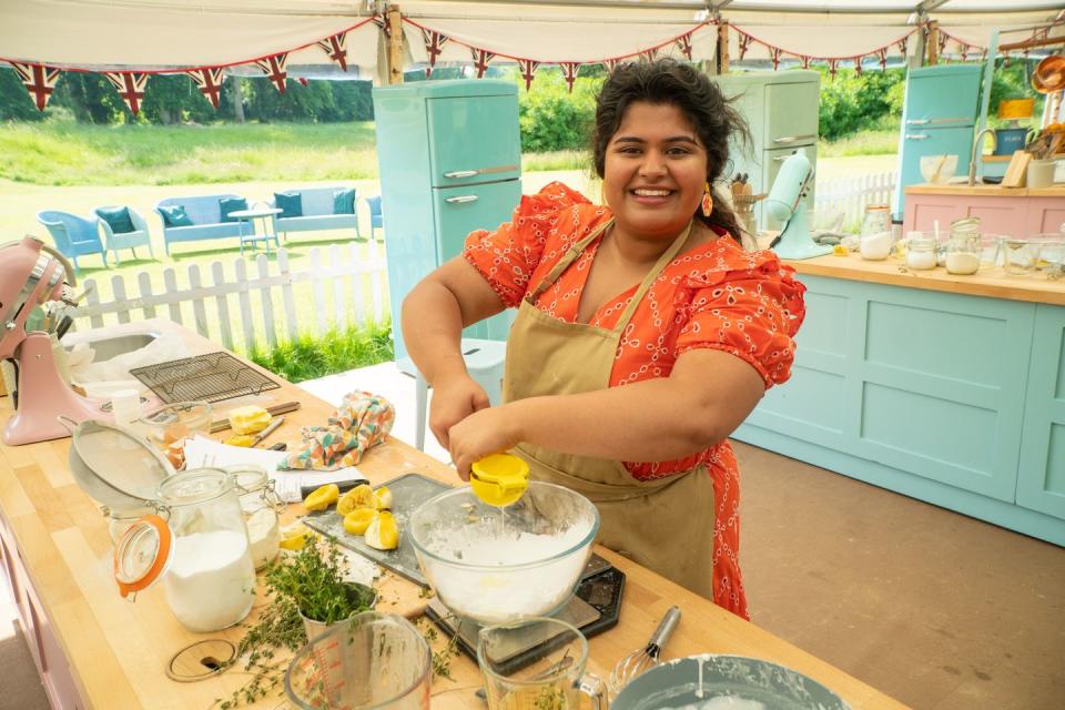 dana, wearing an orange dress and a tan apron, juicing a lemon into a bowl in the great british bake off 2023 during the botanical week episode