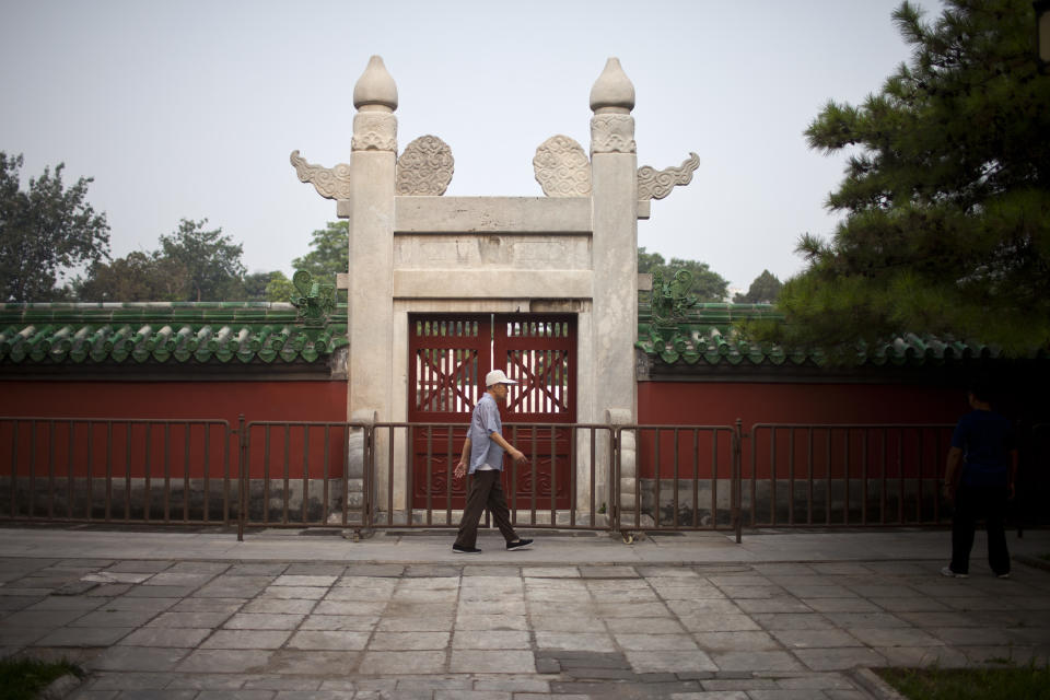 In this Tuesday, July 17, 2012 photo, a man walks past a gate to an ancient circular wall-enclosed altar, where emperors once made offerings to the sun, during his morning exercise at Ritan Park in Beijing, China. The park offers a window on daily Beijing life, starting at dawn with residents practicing tai chi and other exercises like walking backward or rubbing one's back against a tree. (AP Photo/Alexander F. Yuan)