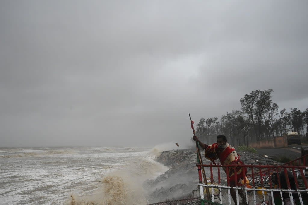 A Hindu priest holds onto a fence at a seafront temple while strong winds batter Balasore district in Odisha (AFP via Getty Images)