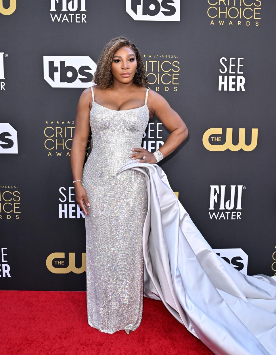 Serena in a silver sparkly spaghetti strap column gown and a long satin cape starting at her hip and onto the ground on one side.