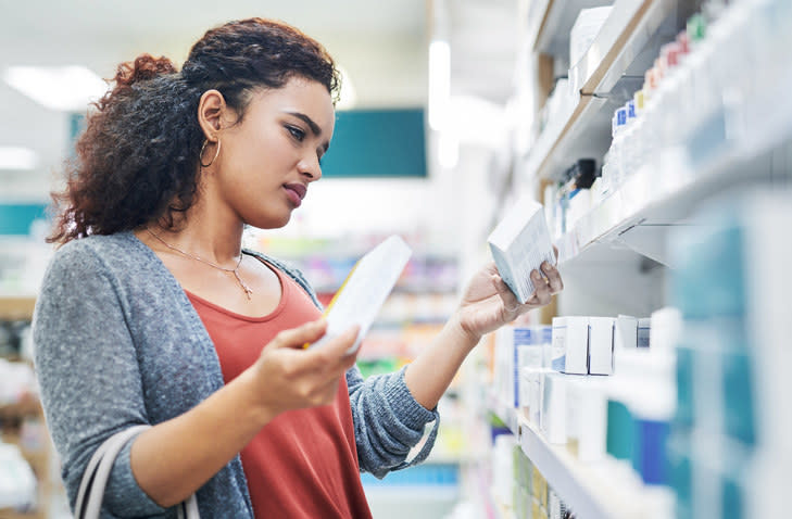 A woman standing in a pharmacy aisle comparing two boxes