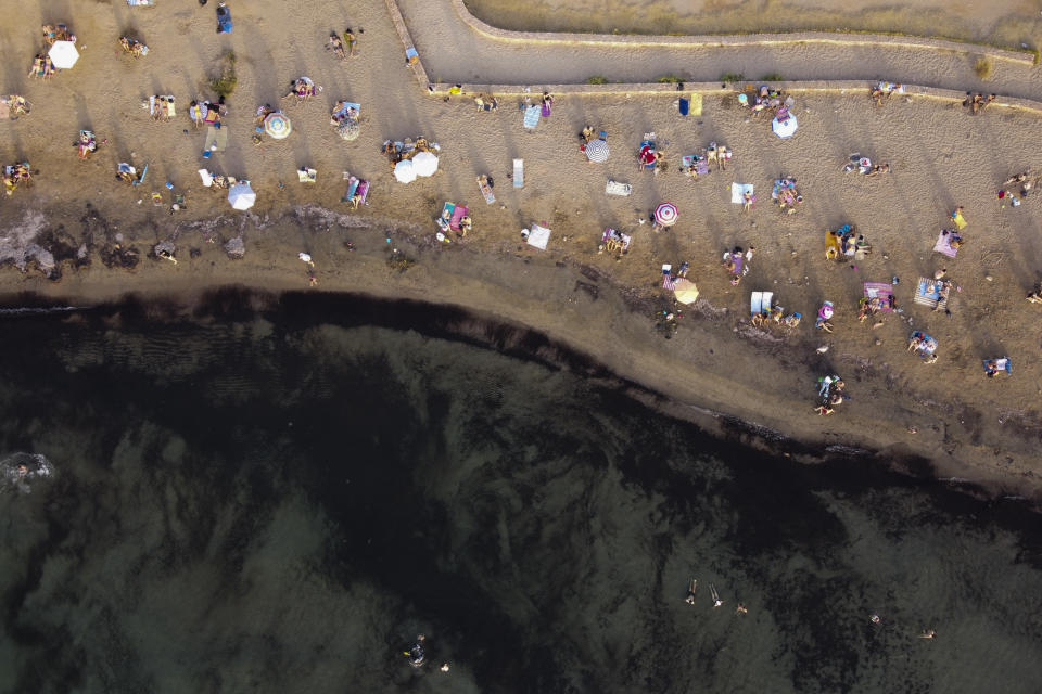 People swim and sunbathe during a heatwave, at a beach of Kavouri suburb, southwest of Athens, Greece, Monday, Aug. 2, 2021. The heat wave is expected to peak Monday, with temperatures inland ranging from 42 to 46 degrees Celsius (107.6 to 114.8 Fahrenheit). Temperatures will remain at 40 Celsius (104 Fahrenheit) or above in much of Greece until at least Friday, meteorologists say. (AP Photo/Michael Varaklas)