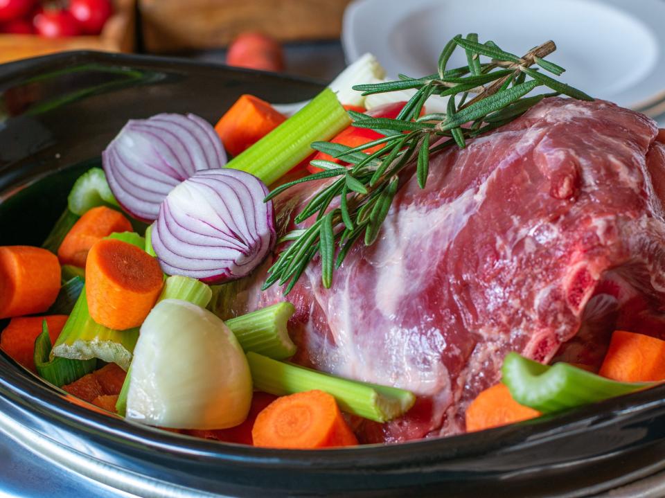 uncooked meat, vegetables, and herbs in a slow cooker