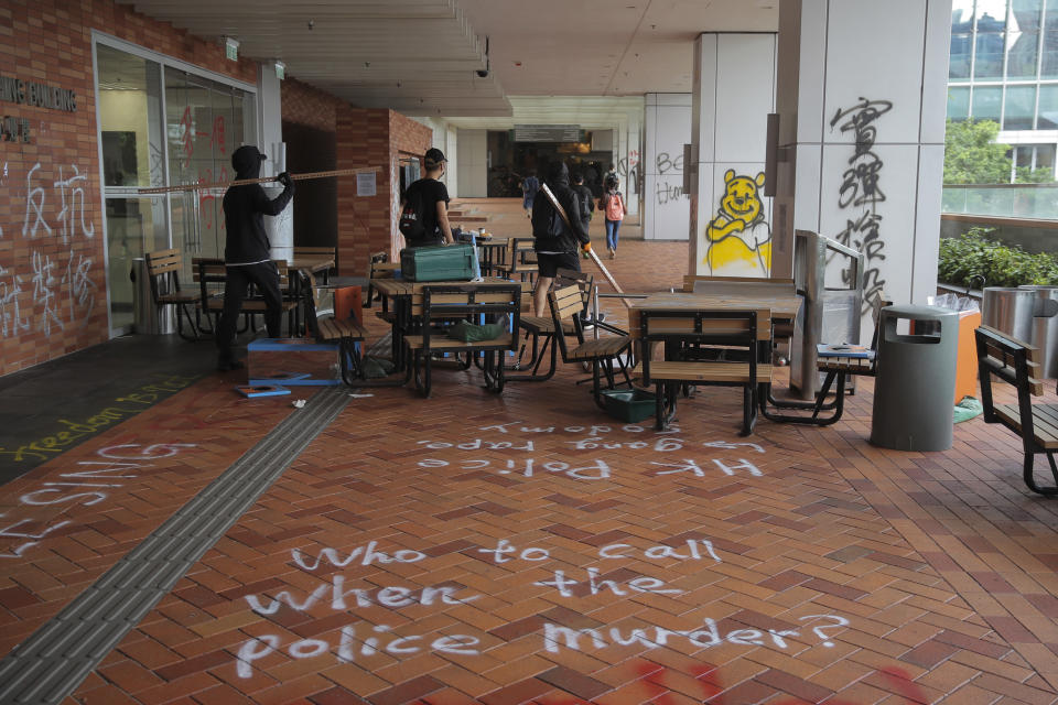 In this Tuesday, Nov. 12, 2019, photo, student protesters walk by the vandalized Hong Kong University as protests continue in Hong Kong. A sharp escalation of violence in Hong Kong has once again raised the question of how China's central government will respond. Experts said national security measures and deployment of the armed forces remain possibilities, though Beijing may just as likely allow destruction to continue unfolding. (AP Photo/Kin Cheung)