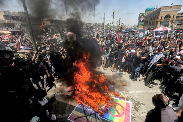 Des partisans du religieux chiite irakien Moqtada al-Sadr brûlent des drapeaux suédois et arc-en-ciel, étendard de la communauté LGBT, lors d'un rassemblement à Sadr City à Bagdad, le 21 juillet 2023 (Murtaja LATEEF)