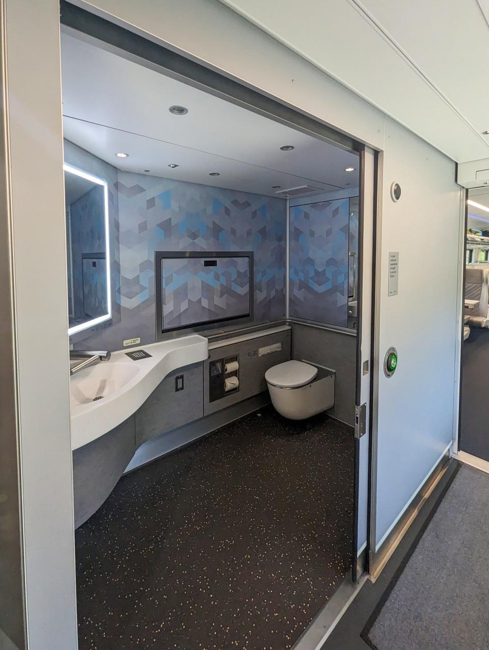 A spacious train restroom in shades of blue and gray is shown.