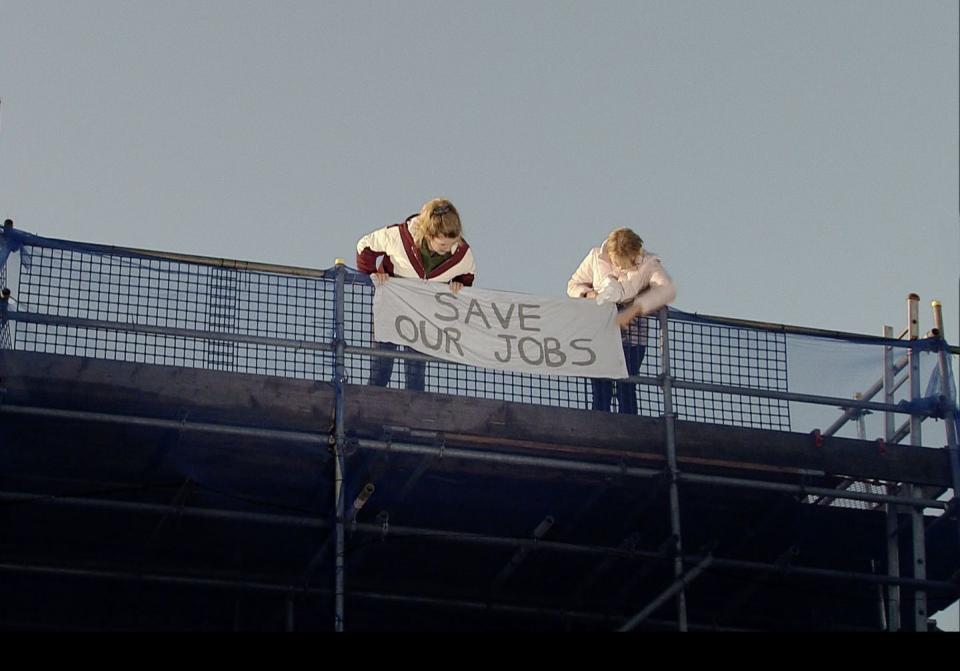 Monday, March 18: Gina and Sally hang a banner on top of the factory