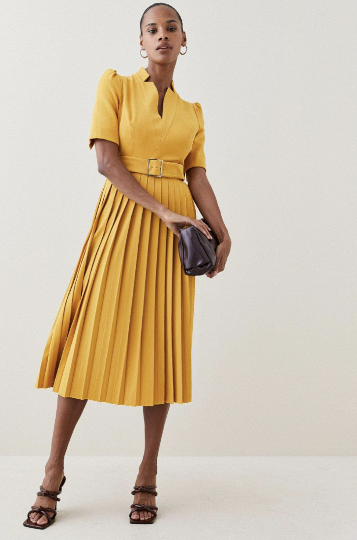 model holding black bag wearing mustard yellow Karen Millen Structured Crepe Forever Pleat Belted Midi Dress (Photo via Karen Millen)