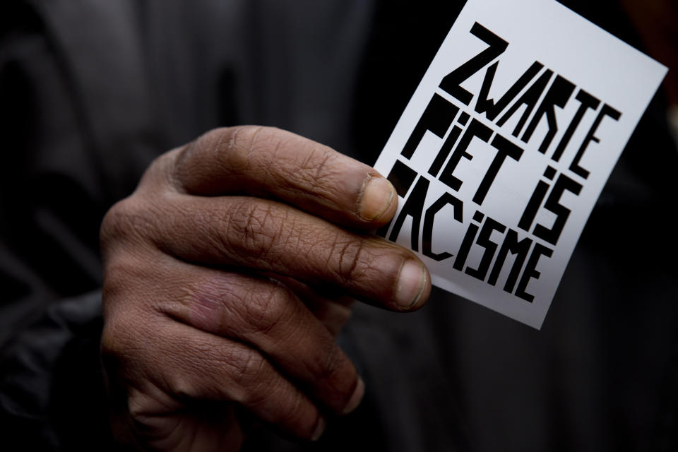 In this Sunday Nov. 17, 2013, file image, a man holds a sign reading "Black Pete is Racism" during the parade of Black Pete, the blackface sidekick of Sinterklaas, the Dutch version of Santa Claus, in Amsterdam, Netherlands. The death of George Floyd at the hands of Minneapolis police officers has sparked a reexamination of many countries' colonial histories, actions and traditions, that often were exalted in the form of statues and other memorials. The Netherlands has been wrestling for years with issues of racism, with much of the debate revolving around the divisive children's character Black Pete, who is usually portrayed by white people wearing blackface makeup at celebrations each December marking Sinterklaas, a Dutch celebration of St. Nicholas. (AP Photo/Peter Dejong, File)