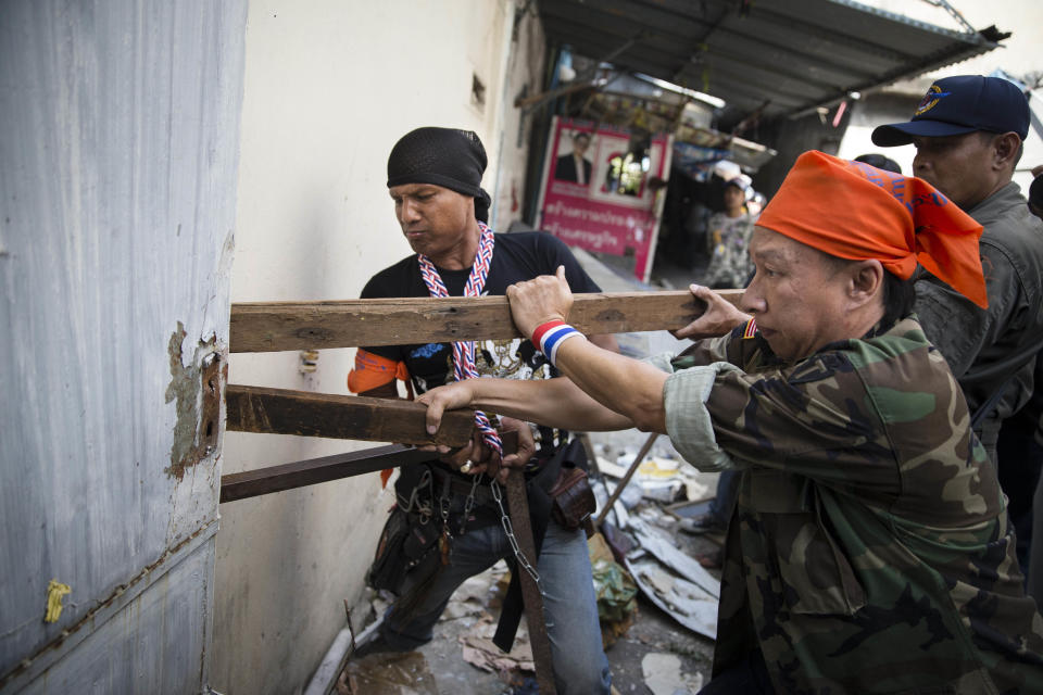 Anti-government protesters break down a door as they search dilapidated buildings near the scene of an explosion in the Pathumwan district, Friday, Jan. 17, 2014, in Bangkok. The march was targeted while on it's way into a protest encampment near the MBK Center. Dozens of people were wounded in the capital Friday when an explosion hit anti-government demonstrators marching through Bangkok in broad daylight, an ominous development that raises tensions in the country’s political crisis and the specter of more bloodshed to come. (AP Photo/John Minchillo)