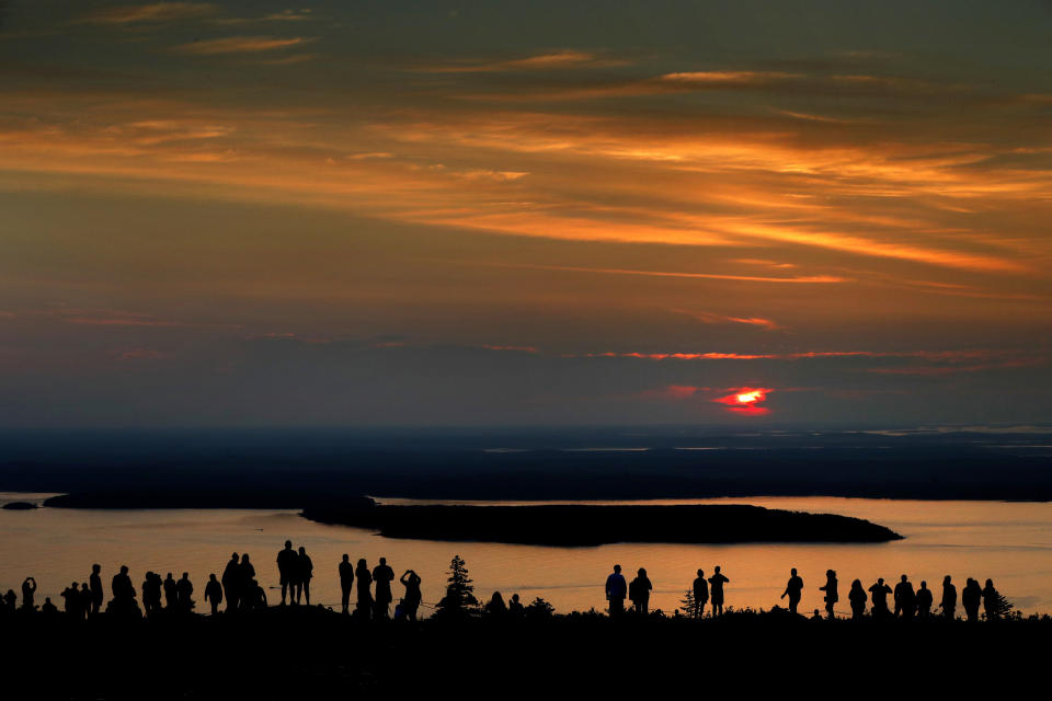 FILE-In this July 31, 2018 file photo, a crowd of early-risers gather near the summit of Cadillac Mountain in Acadia National Park to be among the first in the continental United States to see the sunrise, near Bar Harbor, Maine. The town of Bar Harbor plans to begin charging to park next month. The move comes amid ever-increasing seasonal traffic to Bar Harbor and Acadia National Park, which set a visitation record in 2018.(AP Photo/Robert F. Bukaty, file)