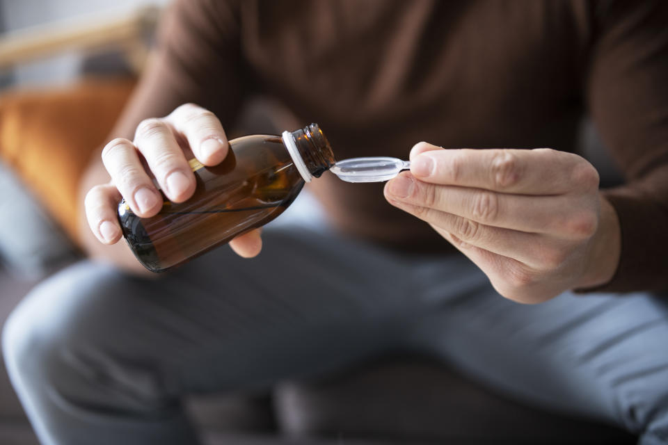 Unrecognisable man pouring cough syrup into spoon.