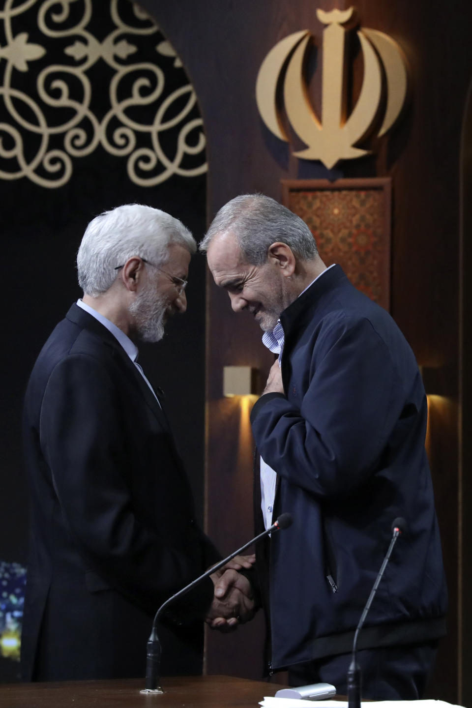 In this picture made available by Iranian state-run TV, IRIB, candidate for the presidential election Saeed Jalili, left, a hard-line former Iranian top nuclear negotiator, and reformist candidate Masoud Pezeshkian shake hands after the conclusion their debate at the TV studio in Tehran, Iran, Monday, July 1, 2024. (Morteza Fakhri Nezhad/IRIB via AP)