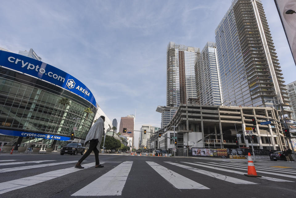 A homeless individual walks across Figueroa Street., in downtown Los Angeles, Friday, Feb. 16, 2024. An unfinished complex of high-rise towers, right, that have recently been vandalized with graffiti and used for dangerous social media stunts after the developer ran out of money have become an embarrassment in a high-profile area that includes Crypto.com Arena, home of major sports teams and events such as the Grammys, as well as the Los Angeles Convention Center and the L.A. Live dining and events complex. (AP Photo/Damian Dovarganes)