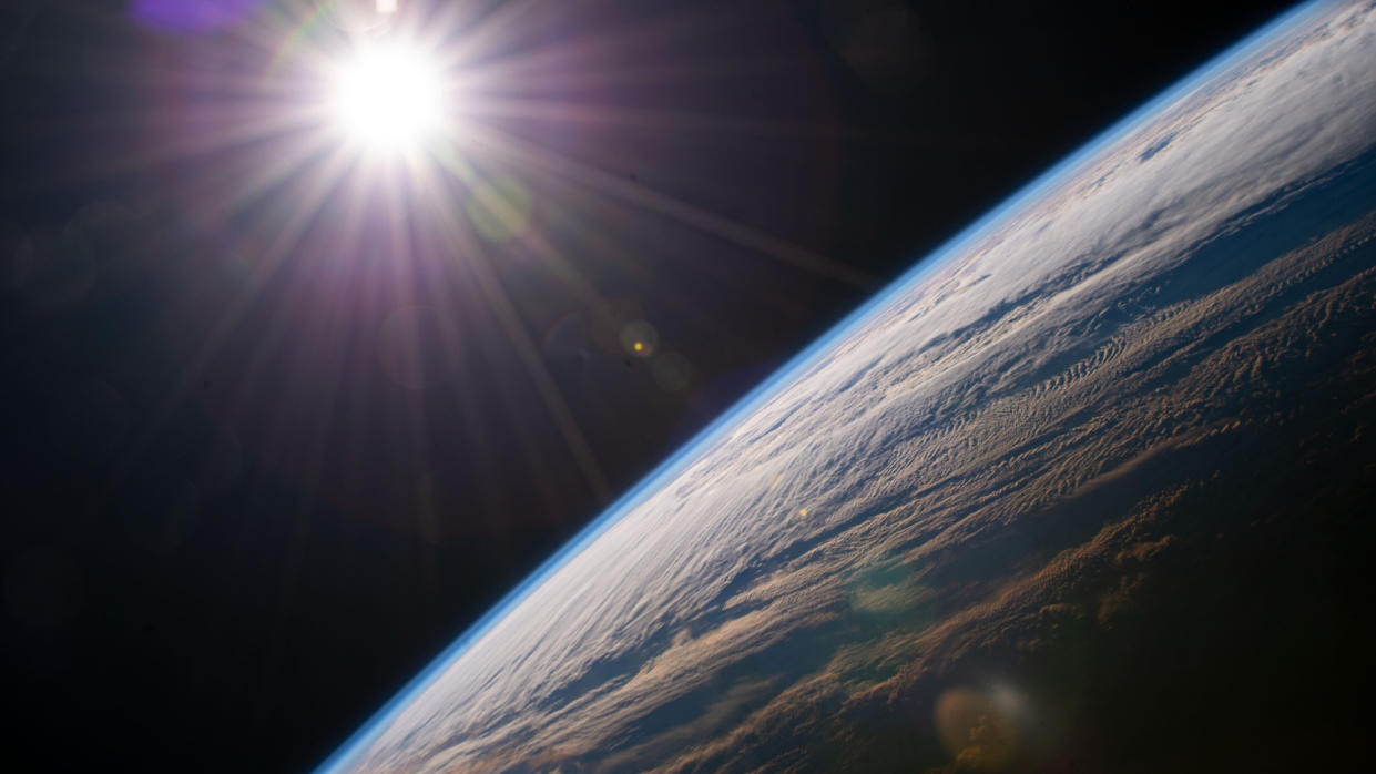  View of the bright sun over the curve of the edge-on earth, with the thinness of the atmosphere apparent. 