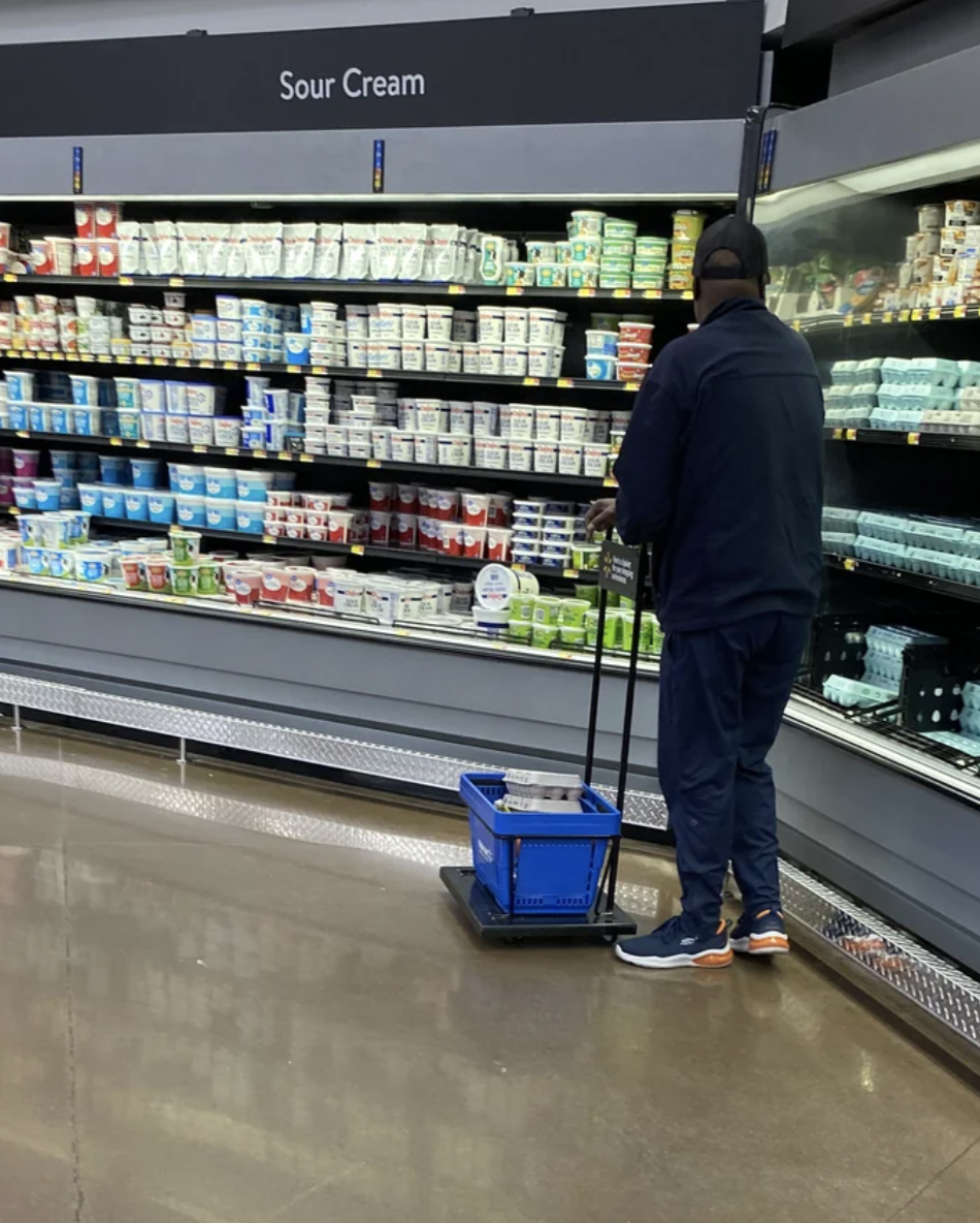 A person in casual clothes shops for sour cream and dairy products in a supermarket aisle