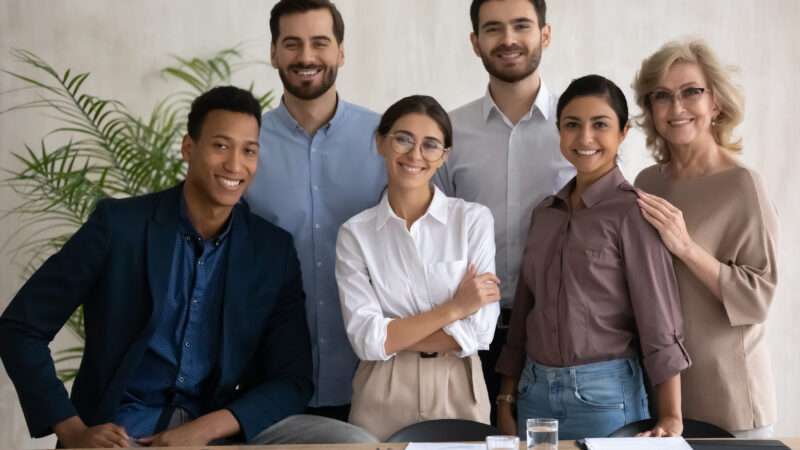 A happy and diverse group of people in a business environment: six people of different ages, races, and genders.