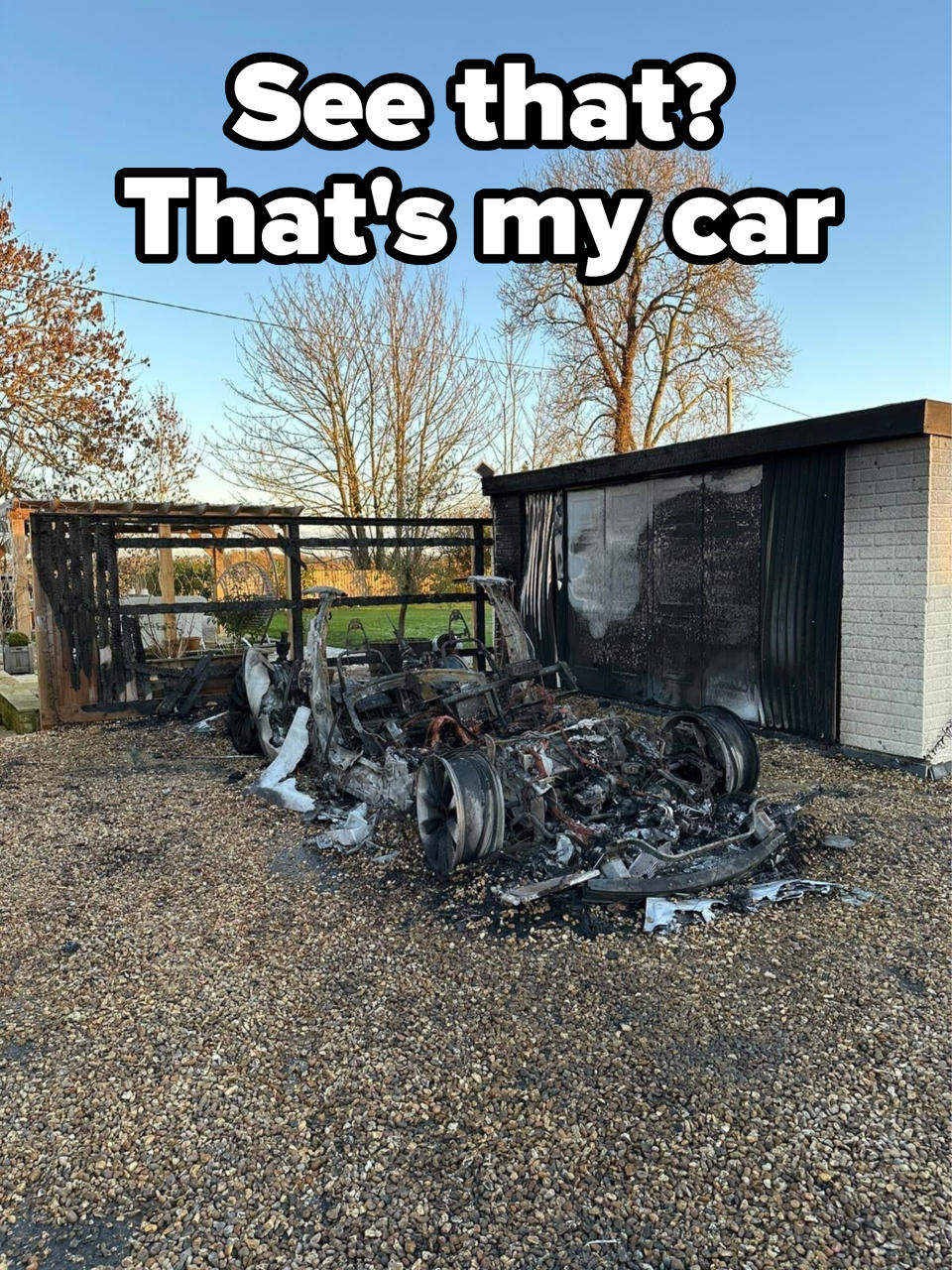 Burnt-out RV remains near a building, evidence of a severe fire incident