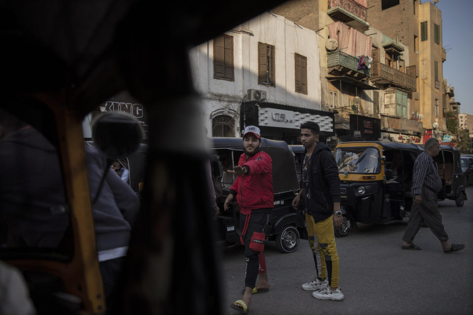 In this Nov. 19, 2019 photo, citizens help tuk-tuk drivers maneuver in traffic at a slum area in Cairo, Egypt. Motorized rickshaws known as tuk-tuks have ruled the streets of Cairo’s slums for the past two decades hauling millions of Egyptians home every day. Now the government is taking its most ambitious stand yet against the polluting three-wheeled vehicles: to modernize the neglected transport system, it plans to replace tuk-tuks with clean-running minivans. (AP Photo/Nariman El-Mofty)