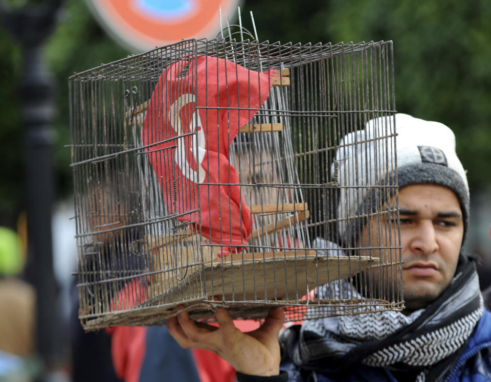 A Tunisian holds a bird cage countaining his national flag during a demonstration to mark the eighth anniversary of the democratic uprising in Tunis, Monday, Jan.14, 2019. Tunisia is marking eight years since its democratic uprising amid deepening economic troubles and simmering anger at the revolution's unfulfilled promises. (AP Photo/Hassene Dridi)