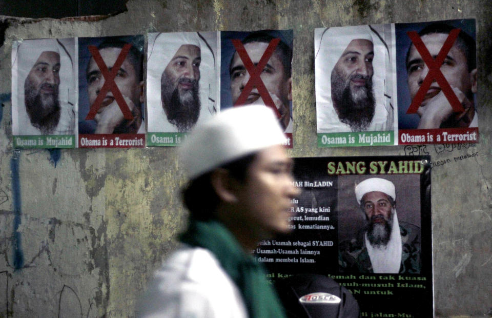 FILE - In this May 4, 2011, file photo, a member of radical group Islam Defenders Front walks past posters of Osama Bin laden and U.S. President Barack Obama, during prayers for the al-Qaida leader at their headquarters in Jakarta, Indonesia. The Islamic Defenders Front, better known for vigilante actions against gays, Christmas decorations and prostitution, has over the past decade and a half repurposed its militia into a force that's as adept at searching for victims buried under earthquake rubble and distributing aid as it is at inspiring fear. (AP Photo/Irwin Fedriansyah, File)