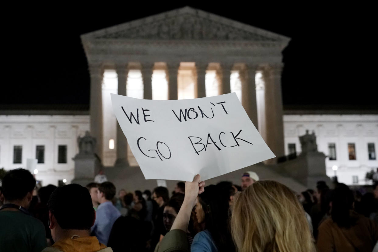 A crowd gathers outside the Supreme Court, with one person holding a sign that reads: We Won&#39;t Go Back.