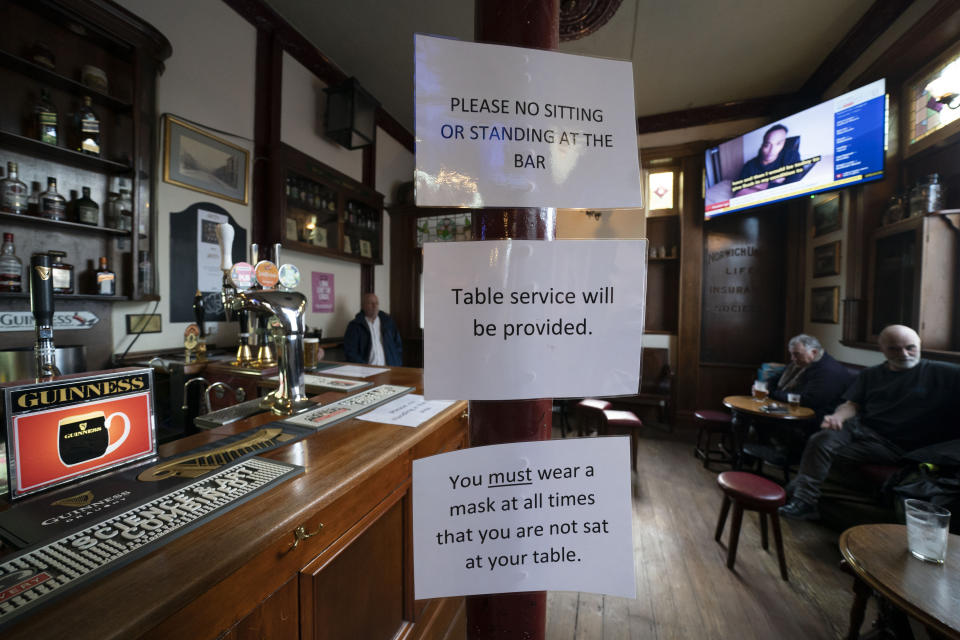 People sit in the Dispensary pub in Liverpool, England, Monday Oct 12, 2020. The British government has carved England into three tiers of risk in a bid to slow the spread of a resurgent coronavirus. The northern city of Liverpool is in the highest category and will close pubs, gyms and betting shops. (AP Photo/Jon Super)