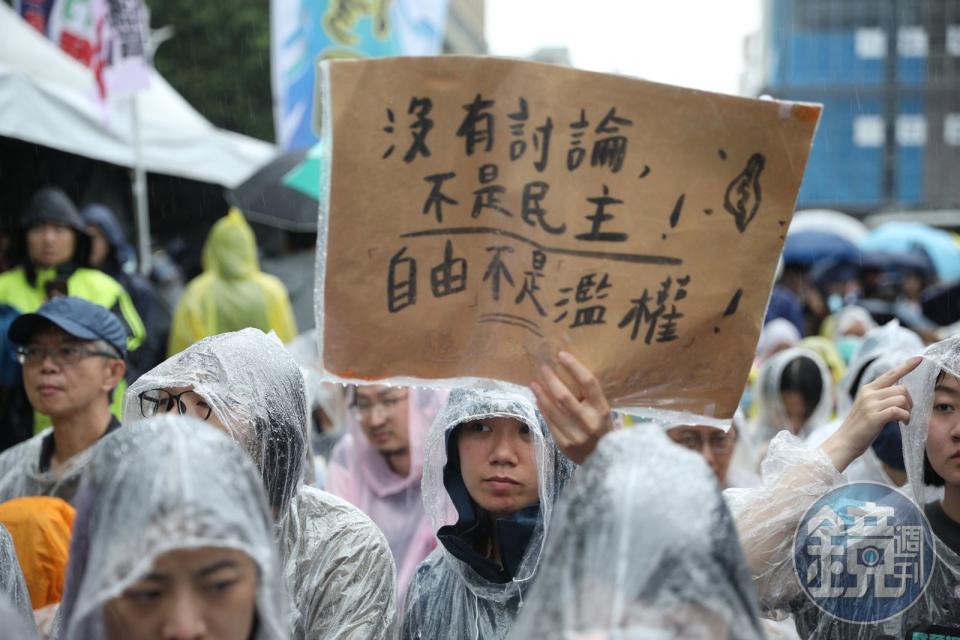 民眾穿著雨衣聚集在立法院外，高舉「沒有討論、不是民主」的口號，抗議藍白強推法案。