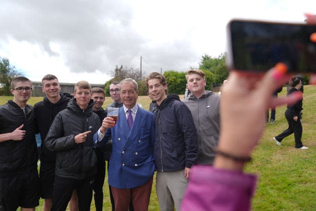 Nigel Farage poses for a selfie with a beer in his hand among a group of young men