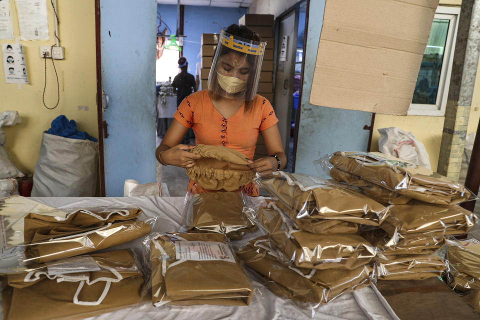 Una mujer con mascarilla y escudo facial para combatir los contagios del nuevo coronavirus comprueba prendas quirúrgicas en una sesión de empaquetado en una fábrica textil, el jueves 28 de mayo de 2020 en la Zona Industrial en Yangón, Myanmar. (AP Foto/Thein Zaw)