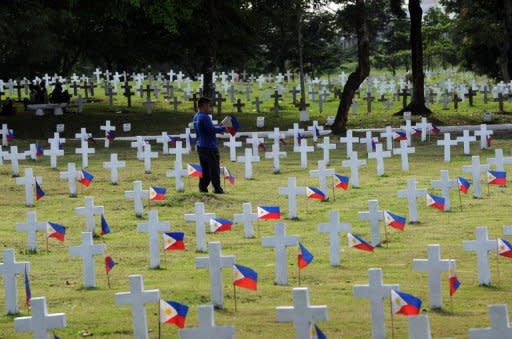 A worker places miniature national flags next to soldiers' graves at the heroes' cemetery in Manila on October 30, 2012. The Catholic Bishops Conference of the Philippines (CBCP) has warned the public against fake priests roaming the cemeteries and reciting prayers for unsuspecting families in exchange for monetary donations