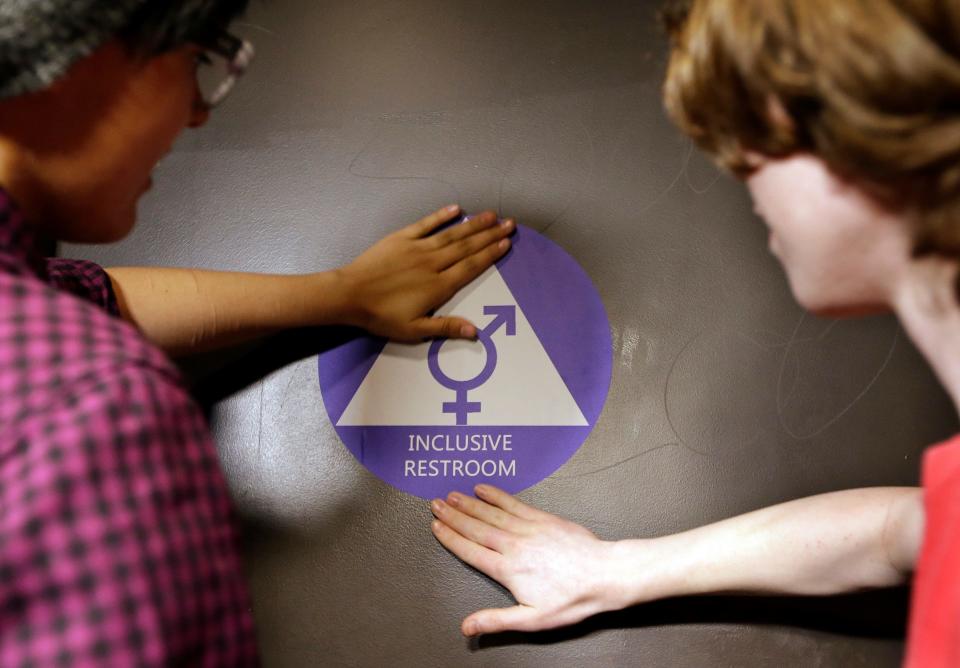 Destin Cramer, left, and Noah Rice place a new sticker on the door at the ceremonial opening of a gender-neutral bathroom at Nathan Hale High School on May 17, 2016, in Seattle.