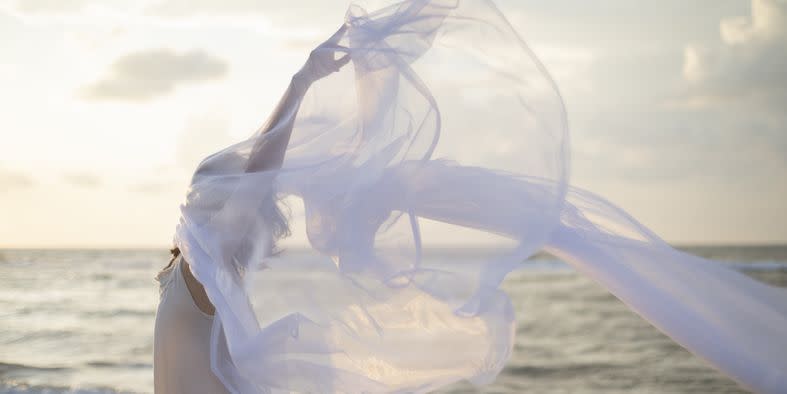 woman holding sheer fabric on a beach in the early morning light