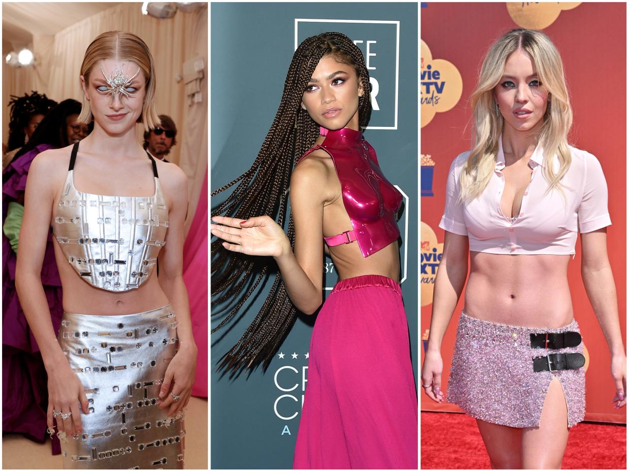 Hunter in a metallic crop top and maxi skirt with a spider accessory in the middle of her face. Zendaya in a dark pink metallic molded bodice with a maxi skirt and long dread braids. Sydney in a cropped button-down top and a sparkly low-waisted miniskirt.