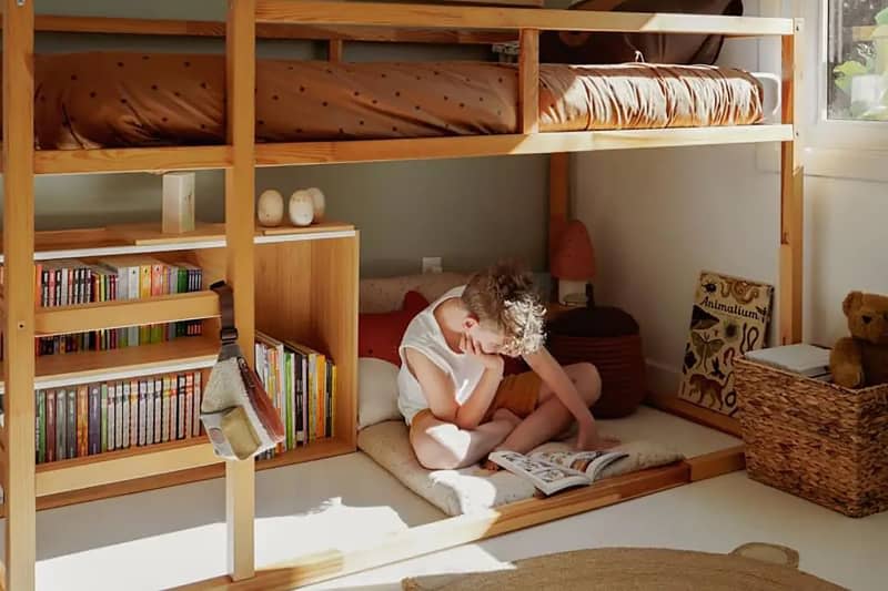 Child sitting on the floor reading under a bunk bed.