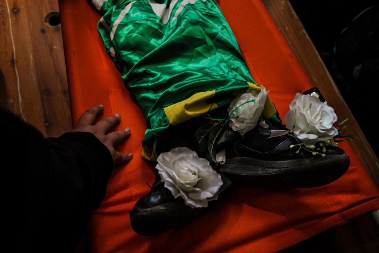 A boy rests his hand near the feet of Amro Najjar, which are decorated with white flowers.