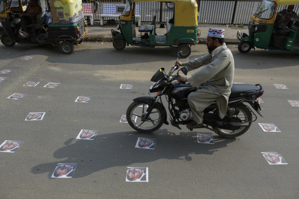 An Indian commuter moves on defaced images of French President Emmanuel Macron pasted by protestors on a road in Ahmedabad, India, Sunday, Nov. 1, 2020. Muslims have been calling for both protests and a boycott of French goods in response to France's stance on caricatures of Islam's most revered prophet. (AP Photo/Ajit Solanki)