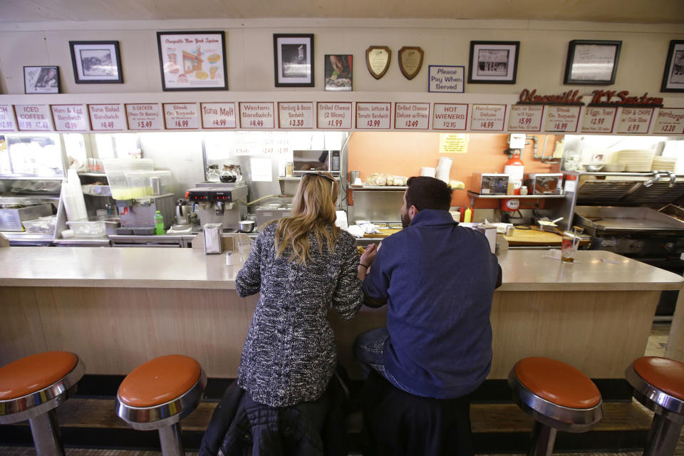 In this Monday, March 3, 2014 photo,Holly Wilson, left, and Ioanni Degaitas eat a lunch of two hot wieners, a loaded cheese burger, a grilled cheese sandwich with bacon and tomato, chile cheese fries, eggs, home fires, coffee milk and black coffee at Olneyville New York System of Providence in Providence, R.I. The James Beard Foundation named the Rhode Island restaurant one of five "American Classics". (AP Photo/Stephan Savoia)