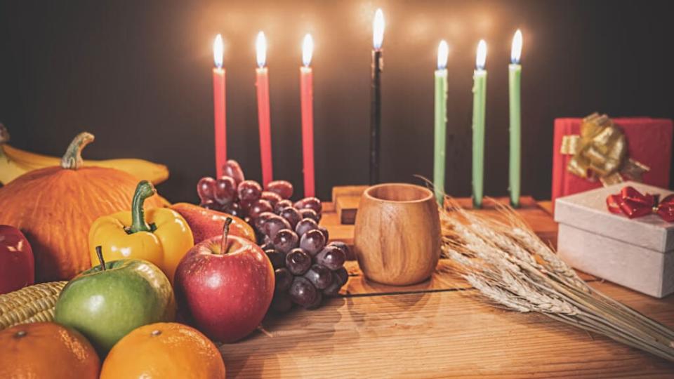 Kwanzaa holiday concept with decorate seven candles red, black and green, gift box, pumpkin,corn and fruit on wooden desk and background.