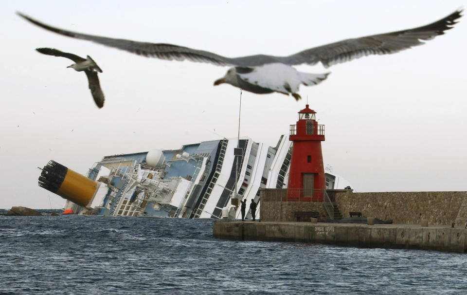 FILE - In this , Monday, Jan. 30, 2012 file photo, seagulls fly in front of the grounded cruise ship Costa Concordia off the Tuscan island of Giglio, Italy. As if the nightmares, flashbacks and anxiety weren't enough, passengers who survived the terrifying grounding and capsizing of the Costa Concordia off Tuscany have come in for a rude shock as they mark the first anniversary of the disaster on Sunday, Jan. 13, 2013. Ship owner Costa Crociere SpA, the Italian unit of Miami-based Carnival Corp., sent several passengers a letter telling them they weren't welcome at the official anniversary ceremonies on the island of Giglio where the hulking ship still rests. Costa says the day is focused on the families of the 32 people who died Jan. 13, 2012, not the 4,200 passengers and crew who survived. (AP Photo/Pier Paolo Cito, File)