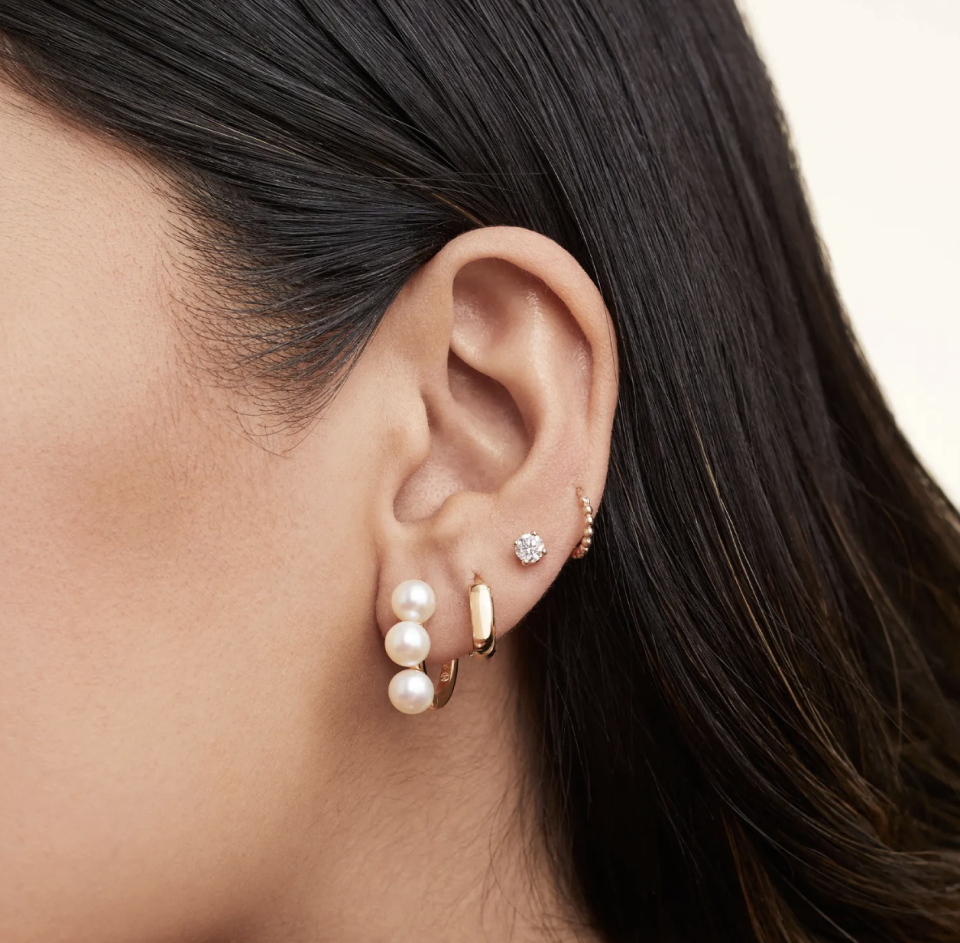 model with black hair wearing Bold Pearl Trio Hoop Earrings and gold and diamond earrings (Photo via Mejuri)