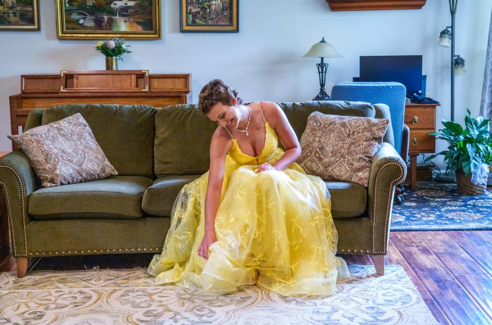 Vivian Eagle, 17, a junior at Avon High School, adjusts her dress as she waits to take photos Saturday, May 13, 2023, ahead of the school's prom. Eagle was a star volleyball player and high jumper with plans to go to college to compete but was diagnosed with osteosarcoma in her left leg in January 2022. She is going to prom with Cade Thompson, a Ben Davis football star who got osteosarcoma, a cancer of the bone, 18 months before her. Eagle's dress gives nod to the cancer ribbon color of osteosarcoma, which is yellow.