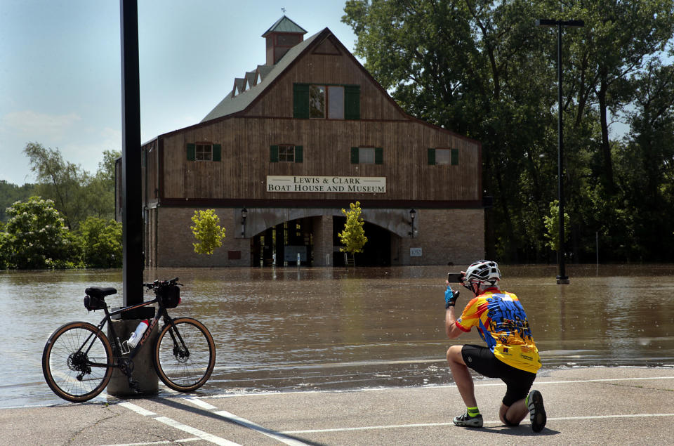 Andy Gaul of Tucson, Arizona photographs his bike in front of the flooded Lewis & Clark Boat House and Museum in Frontier Park on Friday, May 24, 2019. St. Charles officials closed the park and the Katy Trail due to Missouri River flooding, moving a weekend Irish Fest to New Town St. Charles. (Robert Cohen/St. Louis Post-Dispatch via AP)