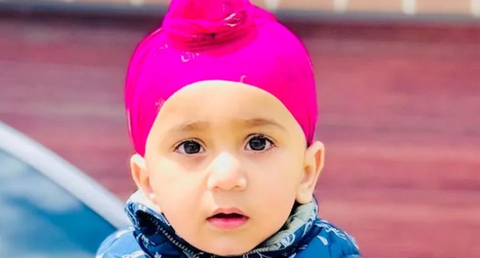11-month old Jugad Singh Bath drowned in a fish tank looks at the camera wearing a pink head wrap and a blue top.  