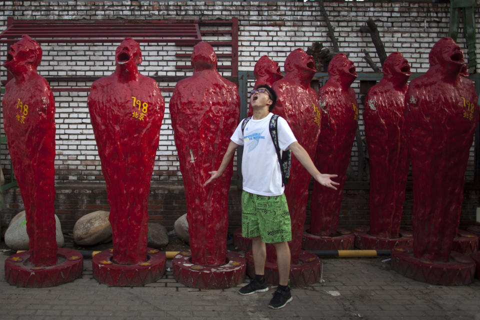 In this Thursday, July 12, 2012 photo, a man poses for photos in front of art pieces at the 798 Art District in Beijing, China. The city's art district, often compared to New York City's Greenwich Village, is a thriving community of about 400 galleries, shops and restaurants on the eastern edge of Beijing housed in a complex of former electronics factories built with the help of East Germany in the 1950s. (AP Photo/Alexander F. Yuan)
