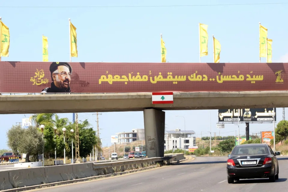 Yellow Hezbollah party flags fly alongside a banner showing the assassinated Hezbollah commander Fuad Shukr on a walkway on the Sidon to Tyre highway in southern Lebanon (AFP via Getty Images)