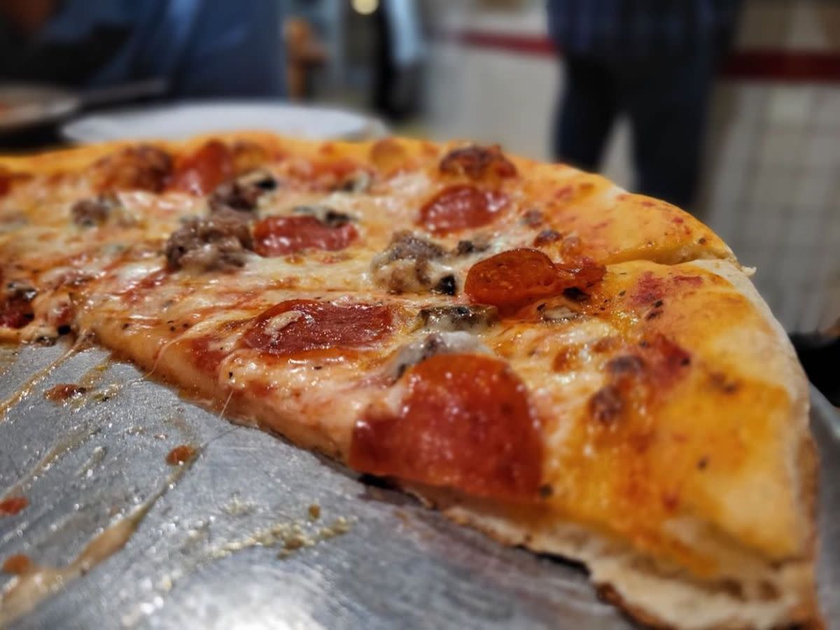 Closeup of half of pepperoni and sausage pizza on a serving tray, Folliero's Italian Food and Pizza, Los Angeles, California, selective focus, restaurant blurred in the background