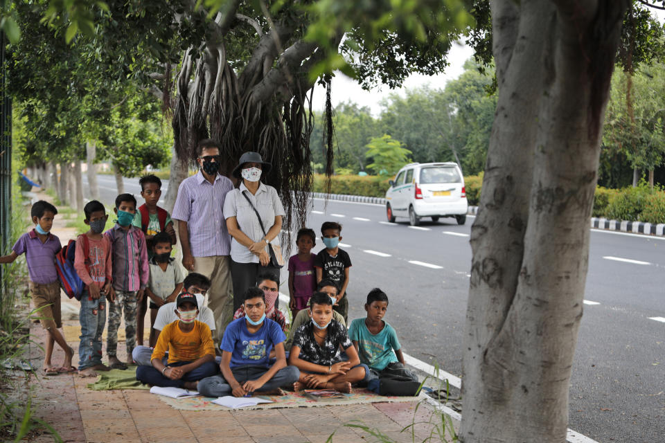 A former diplomat Virendra Gupta and his singer wife Veena Gupta pose for a photograph with underprivileged children whom they teach on a sidewalk in New Delhi, India, on Sept. 3, 2020. The Indian couple are conducting free classes for underprivileged children on a sidewalk in New Delhi with the goal to keep them learning and not left behind when schools reopen. As most schools in India remain shut since late March when the country imposed a nationwide lockdown to curb the spread of COVID-19, many switched to digital learning and taking classes online. (AP Photo/Manish Swarup)