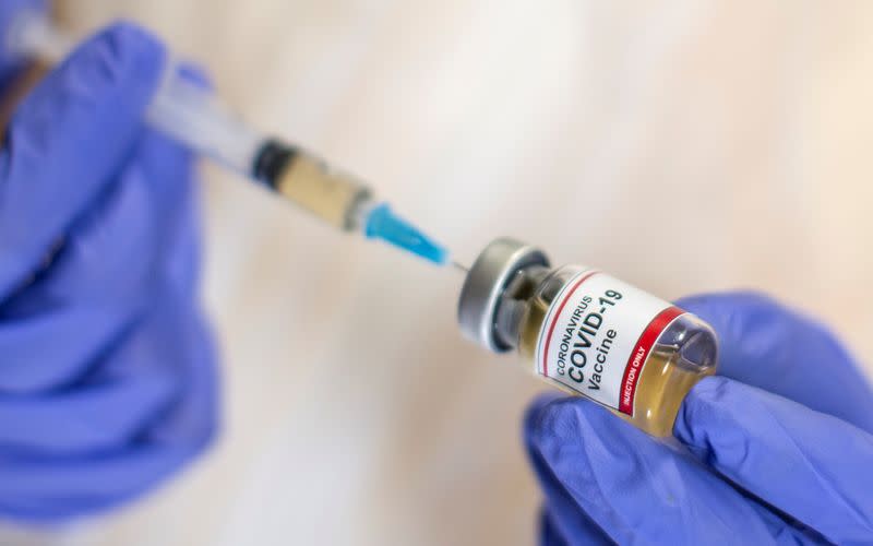 A woman holds a small bottle labeled with a "Coronavirus COVID-19 Vaccine" sticker and a medical syringe in this illustration