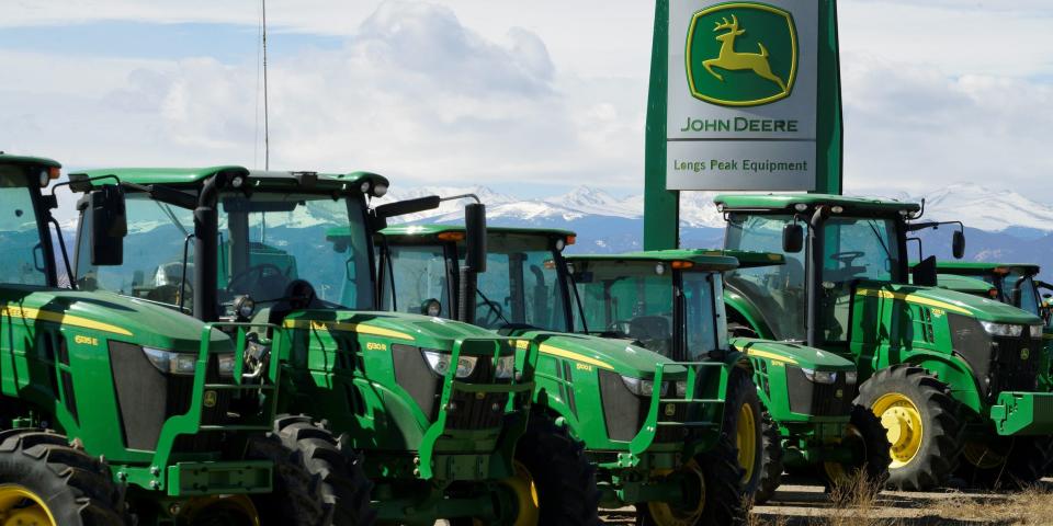 line of green john deere tractors in a dirt lot with snow capped mountains in the background